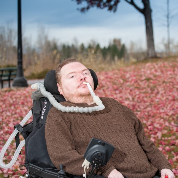 Dustin Hankinson using a breathing tube in his wheelchair outside by a field