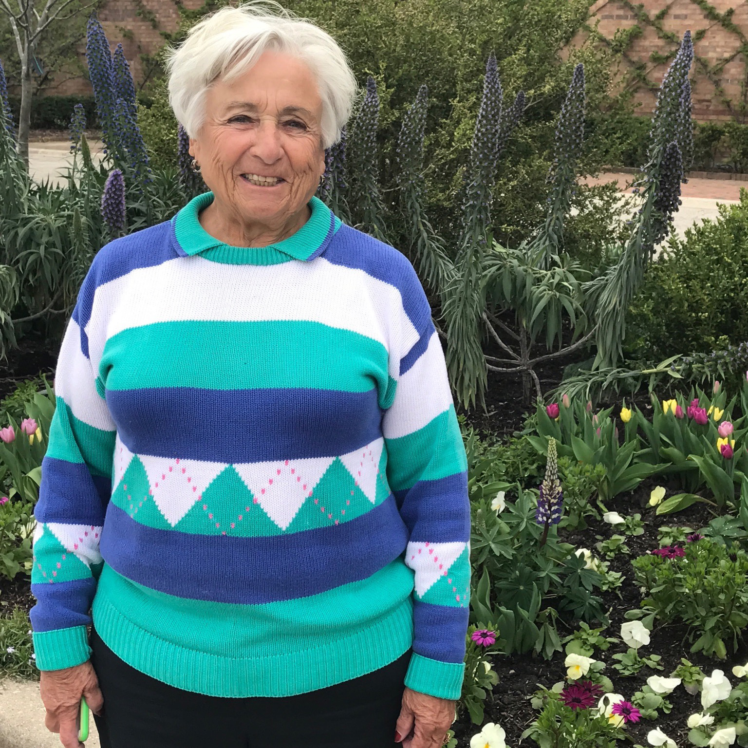 Renée Dushman standing in front of outdoor garden wearing a blue striped sweater.