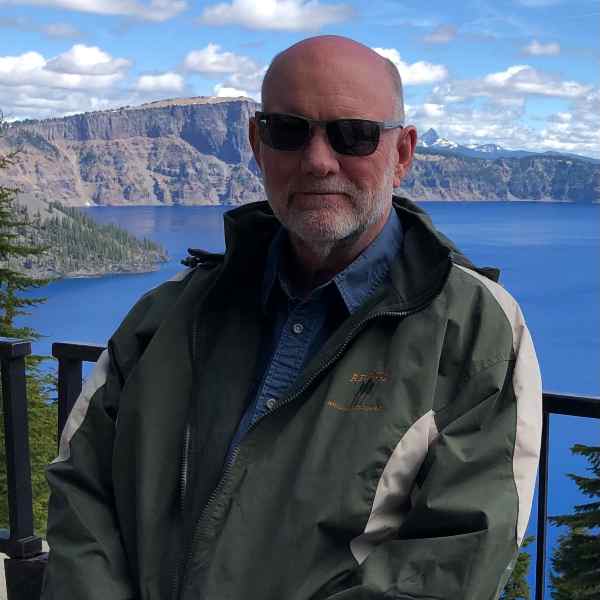 Tom Fitch standing in front of scenic mountainous lake background