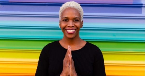 Dr. Sonja Richmond holds her hands together in a prayer shape in front of a rainbow painted wall