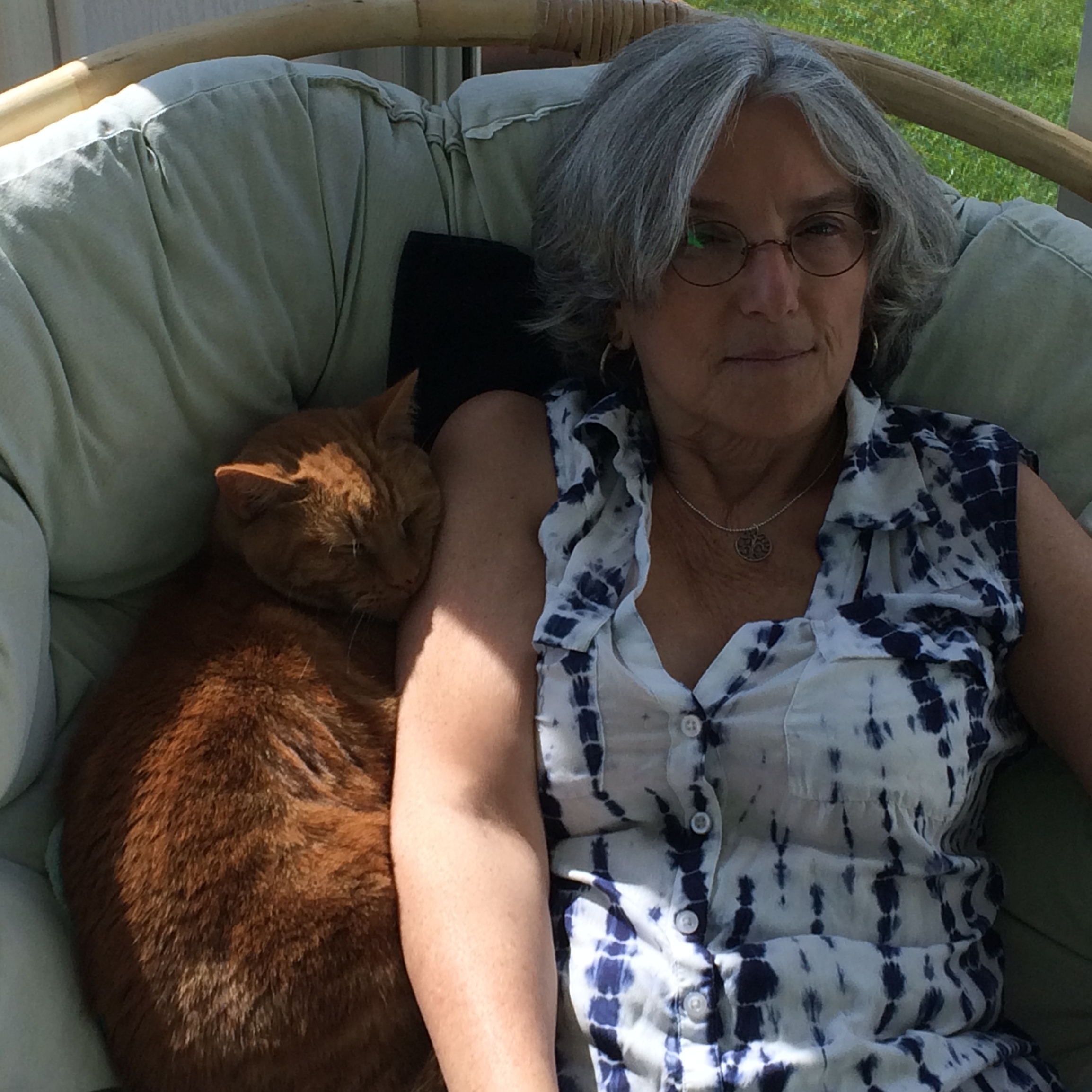 Woman sitting in papasan chair with her cat snuggled up next to her.