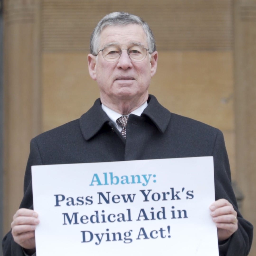 Dr. Robert Milch holding a "Pass New York's Medical Aid in Dying Act" sign